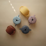 Mushie Snack Cups in yellow, blue, lilac and rust scattered from above