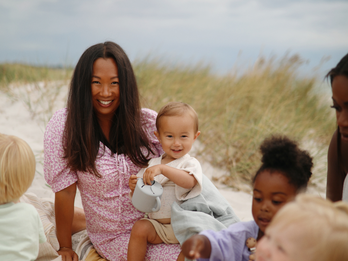 Group of mothers and children with Mushie Snack Cups sitting on a beach