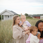 Two mothers with toddlers holding Mushie Snack Cups on a grassy beach