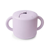 Mushie Snack Cup in Soft Lilac, a lavender silicone cup with two handles and a slotted spill-proof lid