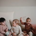 Three toddlers sitting on a bed with Mushie Snack Cups