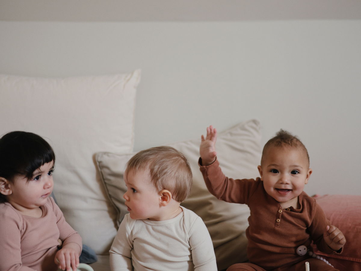 Three toddlers sitting on a bed with Mushie Snack Cups