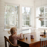 Toddler at a dining table using a Mushie Snack Cup in a bright kitchen