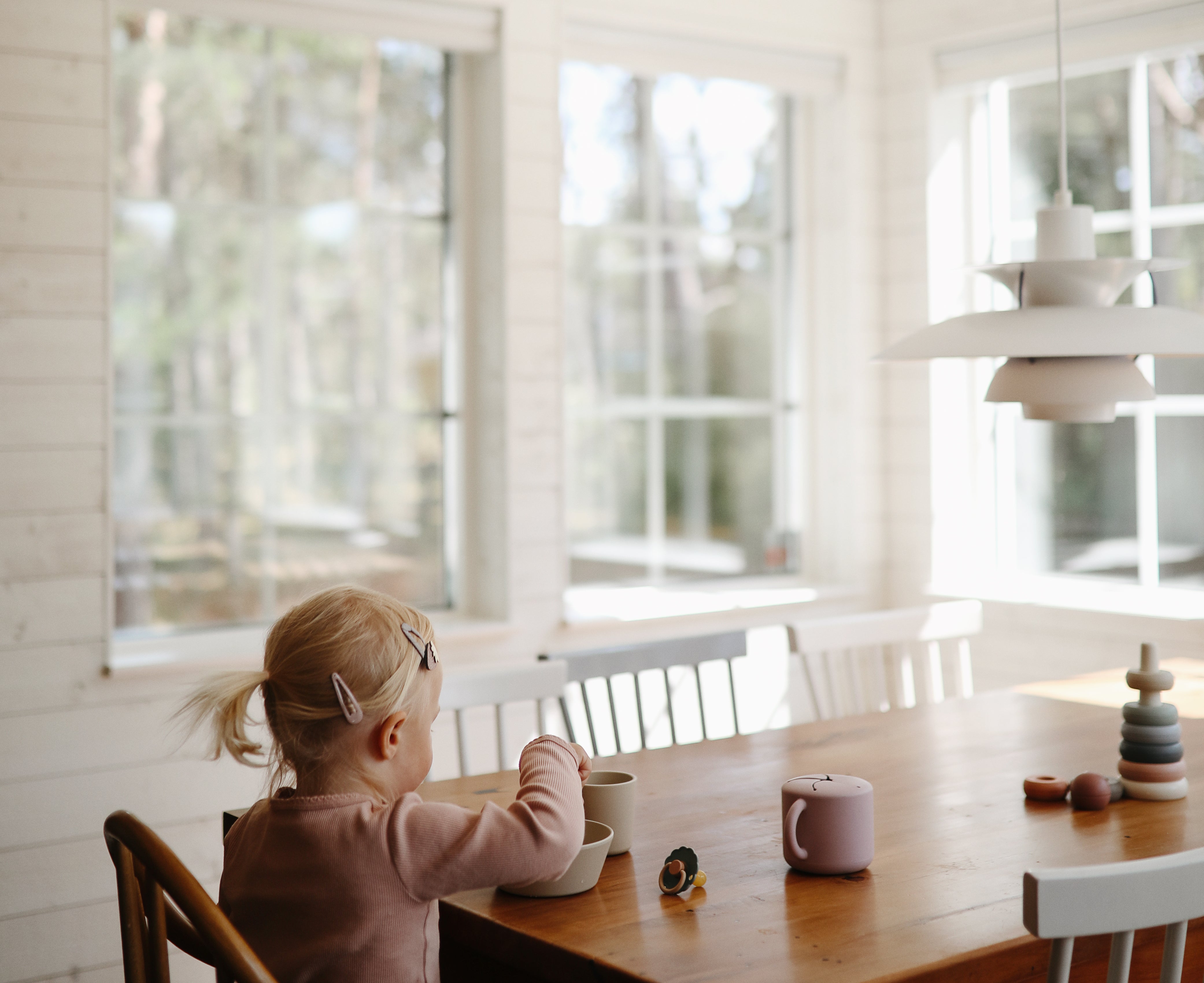 Toddler at a dining table using a Mushie Snack Cup in a bright kitchen