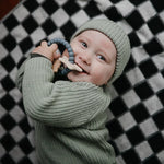 Baby in a green knit outfit chewing the Mushie Space Teething Ring on a checkered blanket