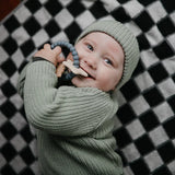 Baby in a green knit outfit chewing the Mushie Space Teething Ring on a checkered blanket