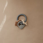 Mushie Space Teething Ring on a tan surface in soft light