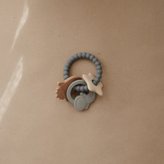 Mushie Space Teething Ring on a tan surface in soft light