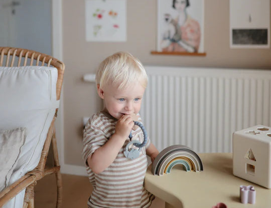 Toddler chewing the Mushie Space Teething Ring in a playroom