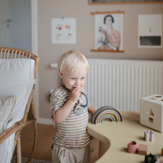 Toddler chewing the Mushie Space Teething Ring in a playroom