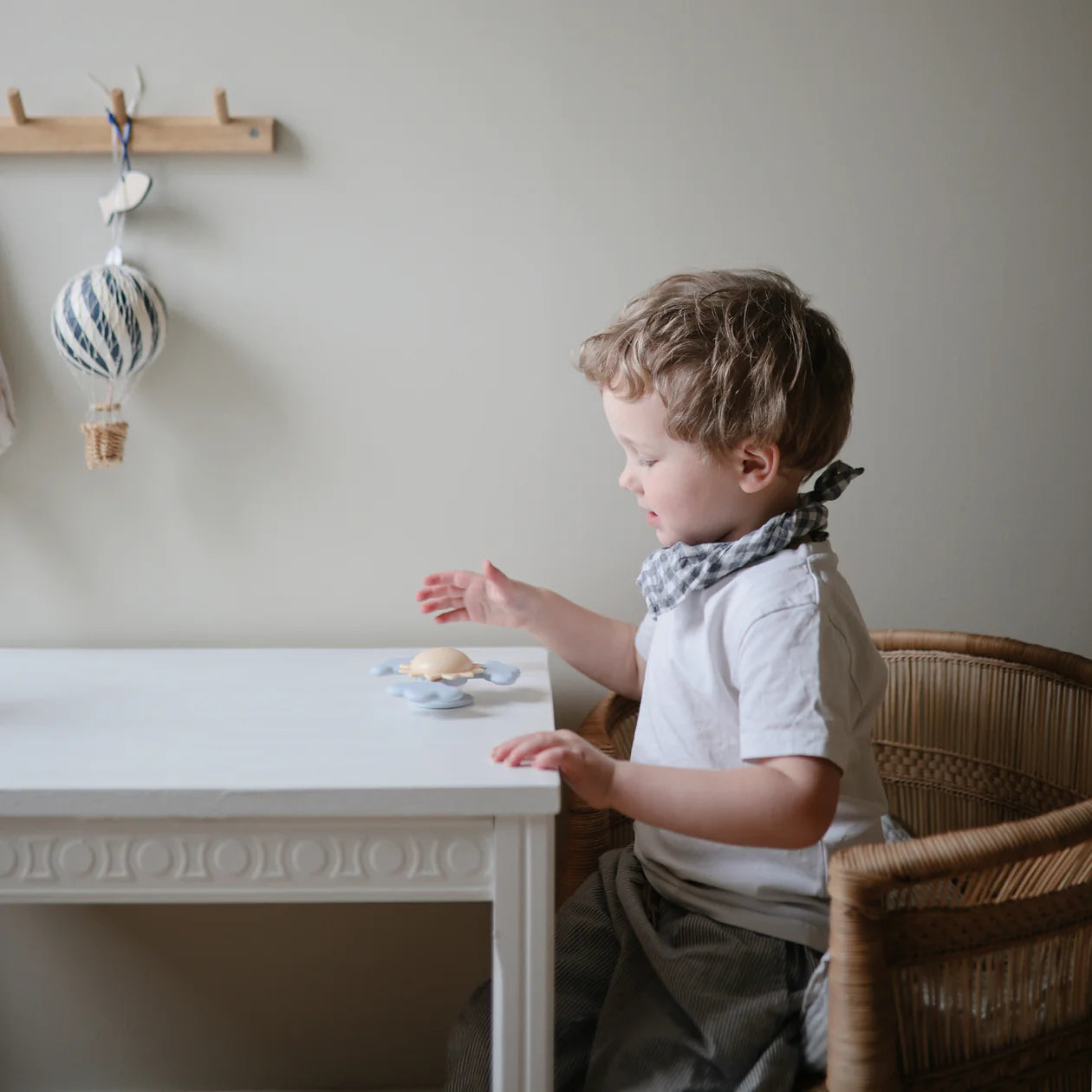 Toddler at a white table playing with the Mushie Sunshine Suction Spinner Toy