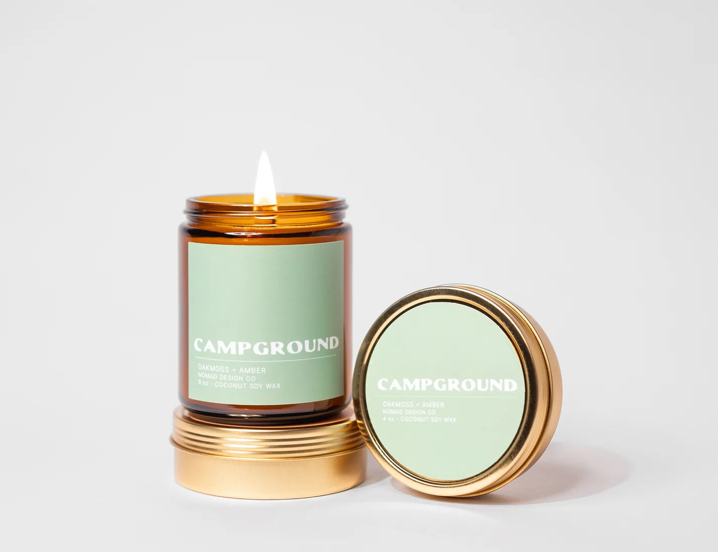 Nomad Design Co Campground Travel Tin Candle, a lit gold tin candle with a green label and its lid