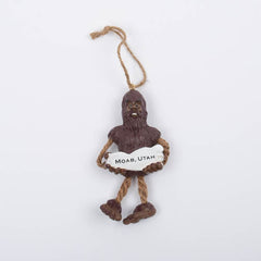 Sasquatch Ornament, brown sasquatch holding a Moab, Utah sign, with dangling rope legs and a twine hanger