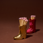 Paddywax Cowboy Boot Match Holders in Gold Metallic and Red & Pink Flame side by side with matches