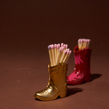 Paddywax Cowboy Boot Match Holders in Gold Metallic and Red & Pink Flame side by side with matches