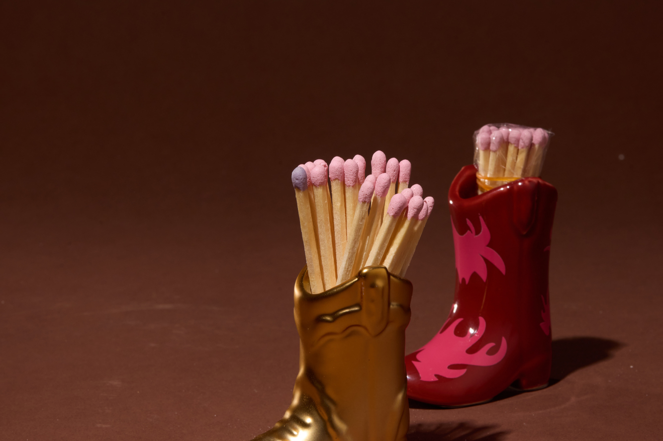 Paddywax Cowboy Boot Match Holders in Gold Metallic and Red & Pink Flame side by side with matches