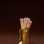 Paddywax Cowboy Boot Match Holder in Gold Metallic with pink-tipped matches on a dark background
