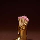 Paddywax Cowboy Boot Match Holder in Gold Metallic with pink-tipped matches on a dark background
