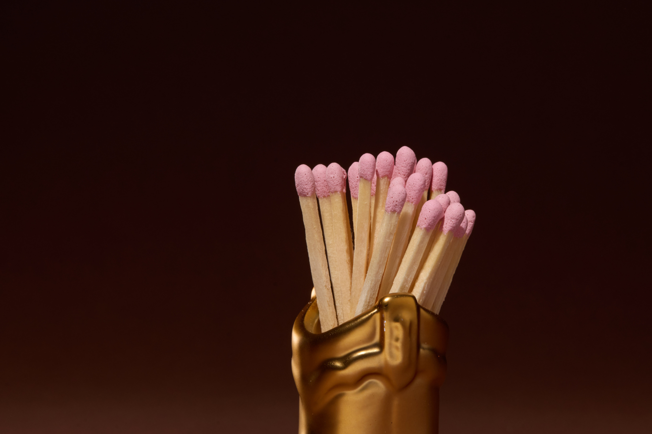 Paddywax Cowboy Boot Match Holder in Gold Metallic with pink-tipped matches on a dark background