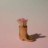Paddywax Cowboy Boot Match Holder in Gold Metallic with matches on a pink background