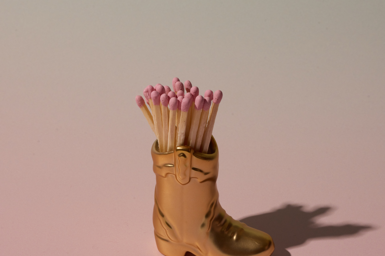 Paddywax Cowboy Boot Match Holder in Gold Metallic with matches on a pink background