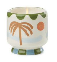 Cream ceramic candle hand painted with a terracotta palm tree, orange sun and green scalloped rim