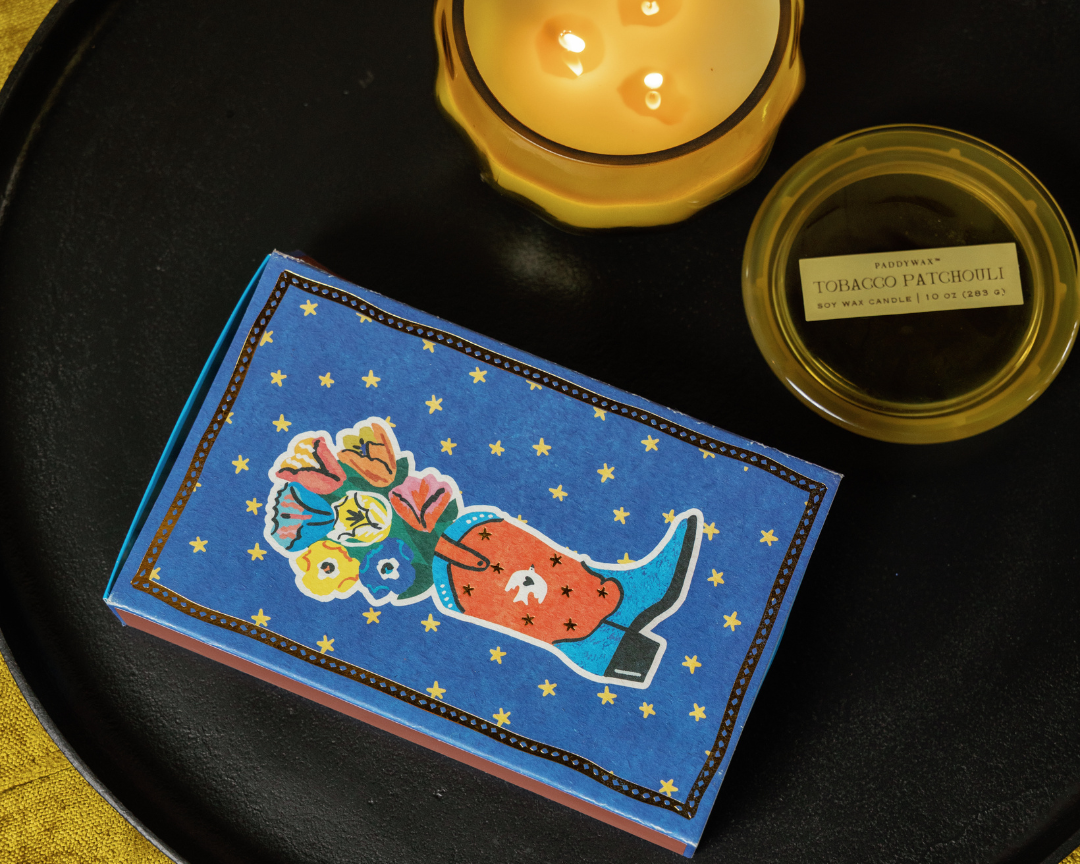 Cobalt blue Paddywax matchbox with a cowboy boot holding flowers and gold stars, second view