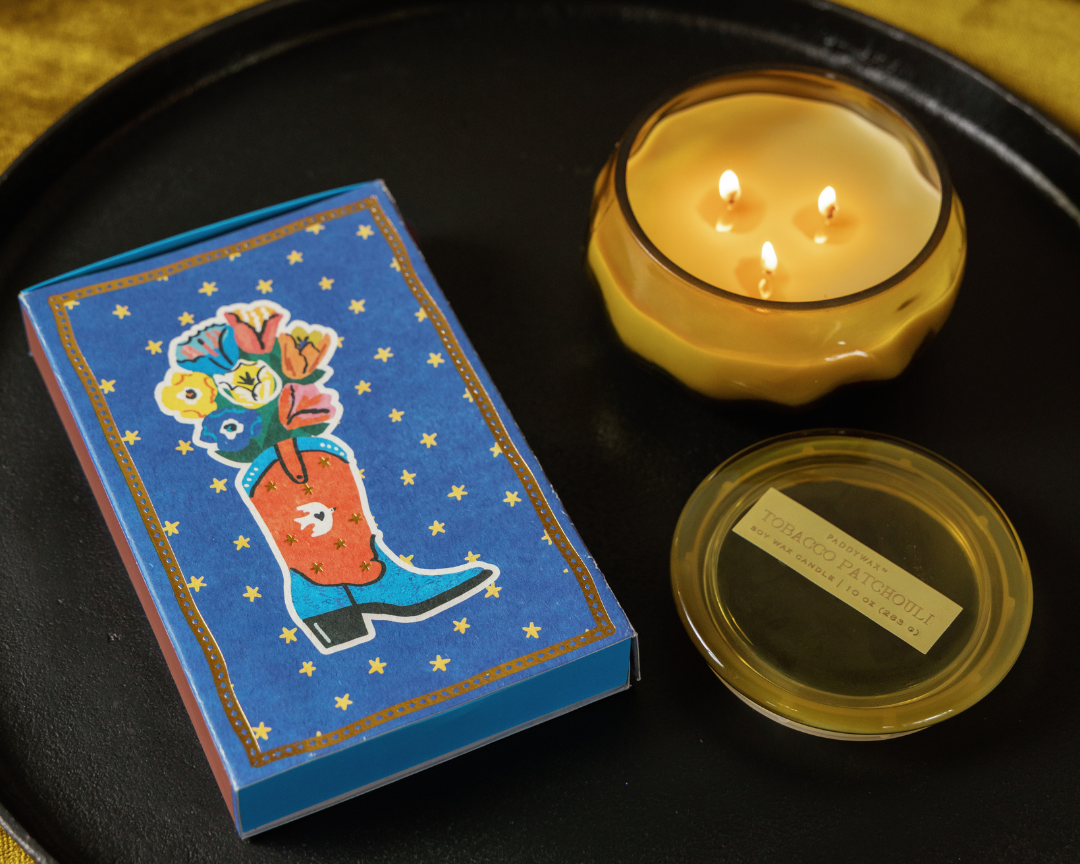 Cobalt blue Paddywax matchbox with a cowboy boot holding flowers and gold stars