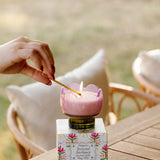 Hand lighting the Paddywax Tulip Glass Candle in pink at an outdoor table