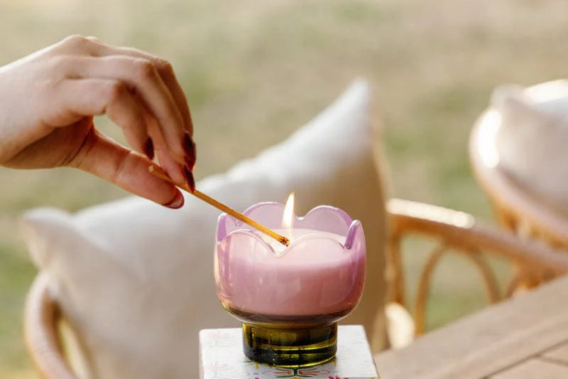 Hand lighting the Paddywax Tulip Glass Candle in pink at an outdoor table