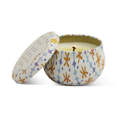 Round Paddywax tin candle printed with ochre, blue and purple flowers, lid resting beside it