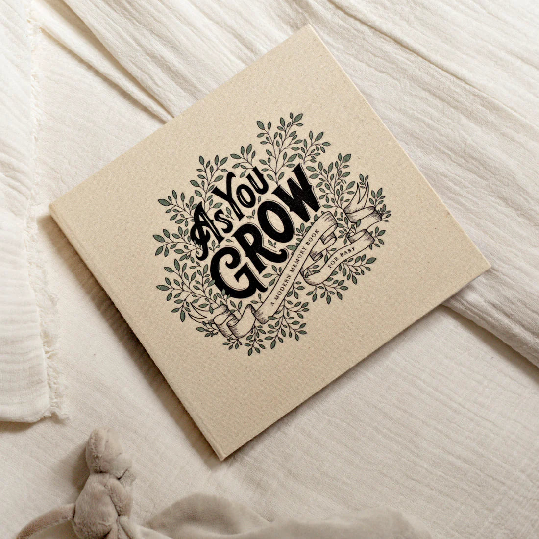 Paige Tate & Co As You Grow Memory Book lying on a soft cream blanket