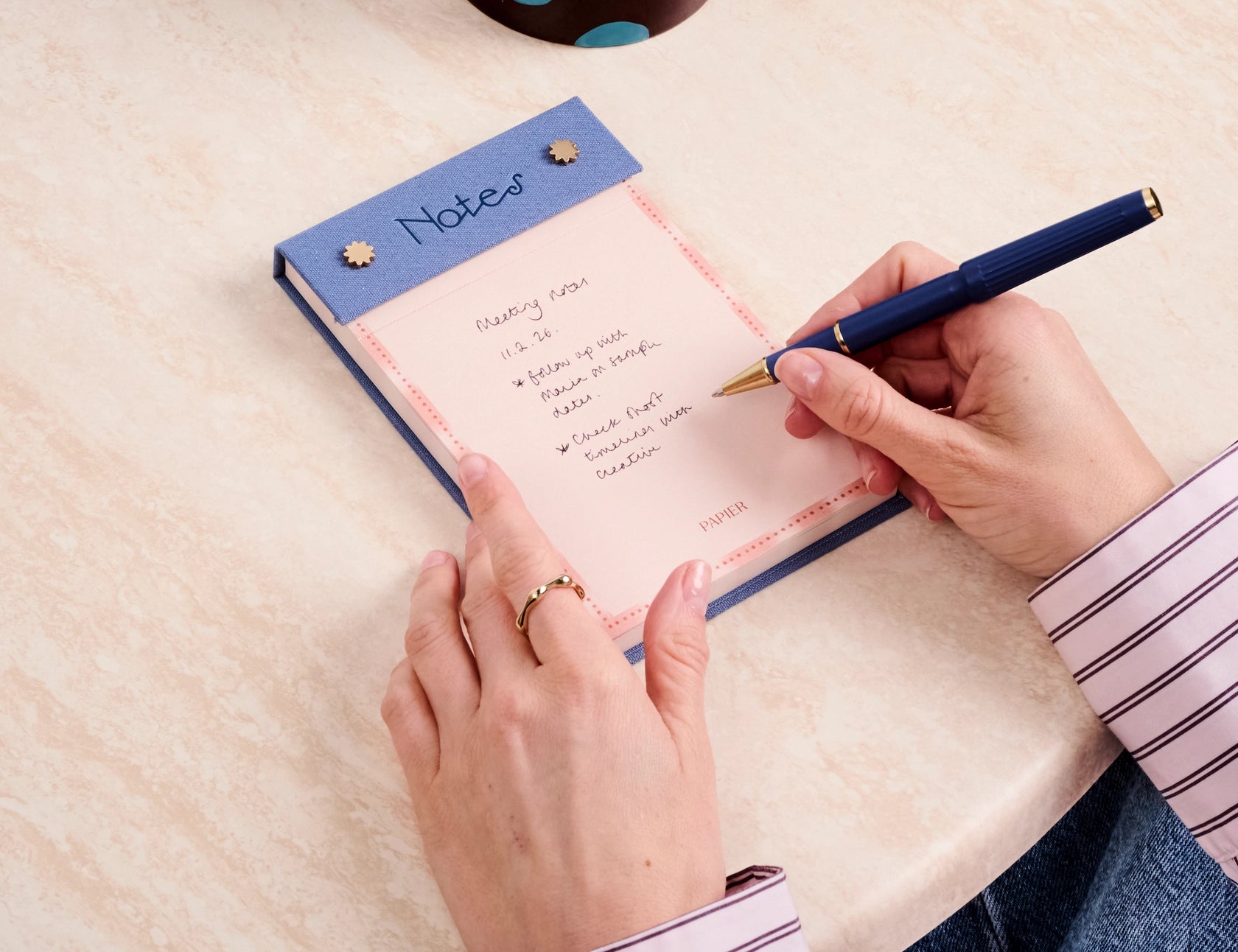 Hand writing on the Papier Fabric Hardcover Notepad in pink at a desk