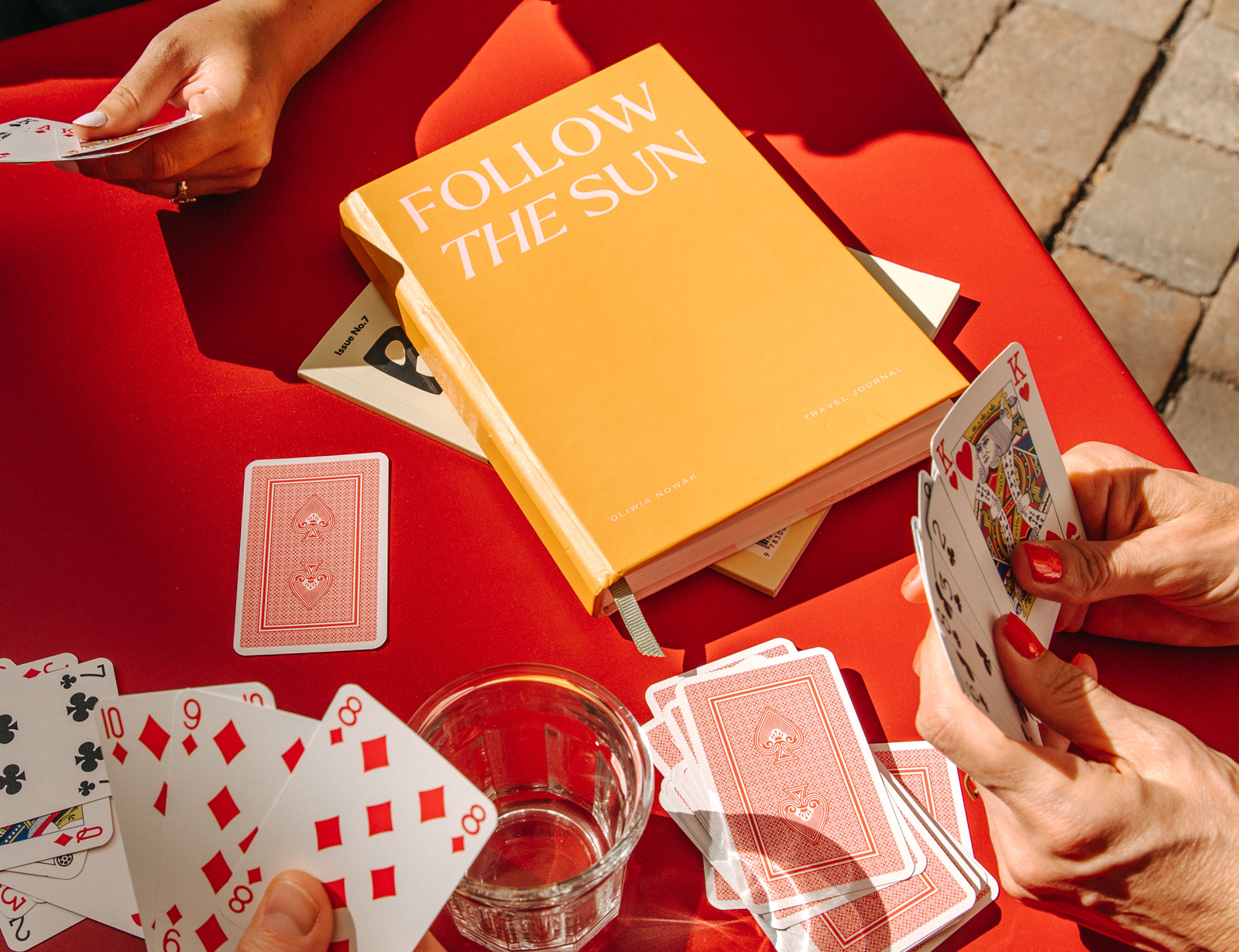 Papier Follow the Sun Travel Journal on a red table with playing cards and a drink