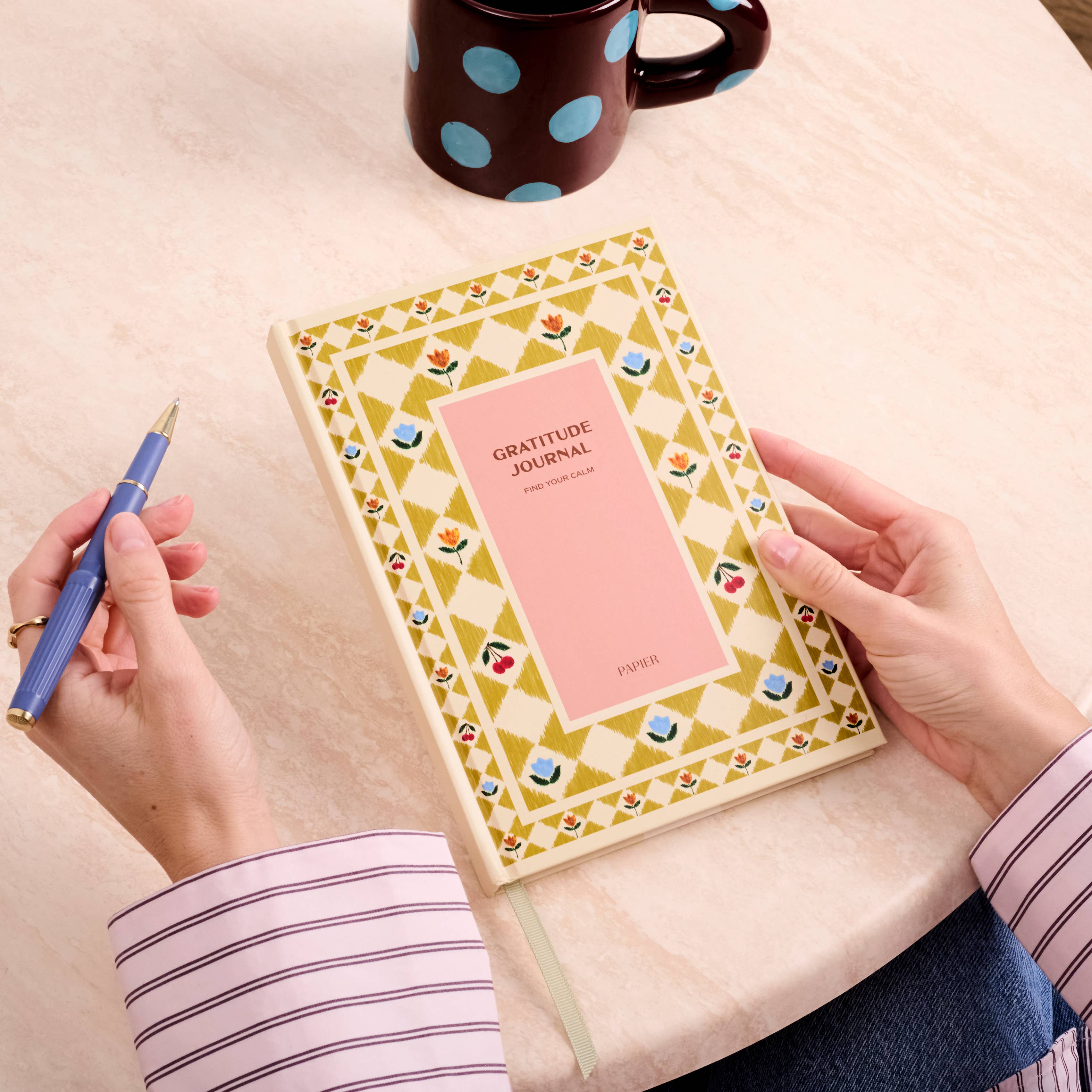 Hands holding the Papier Guided Gratitude Journal A5 Folk Garden at a table with a pen