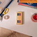 Papier High Energy Fineliners Set in its yellow box on a desk with scissors and tape