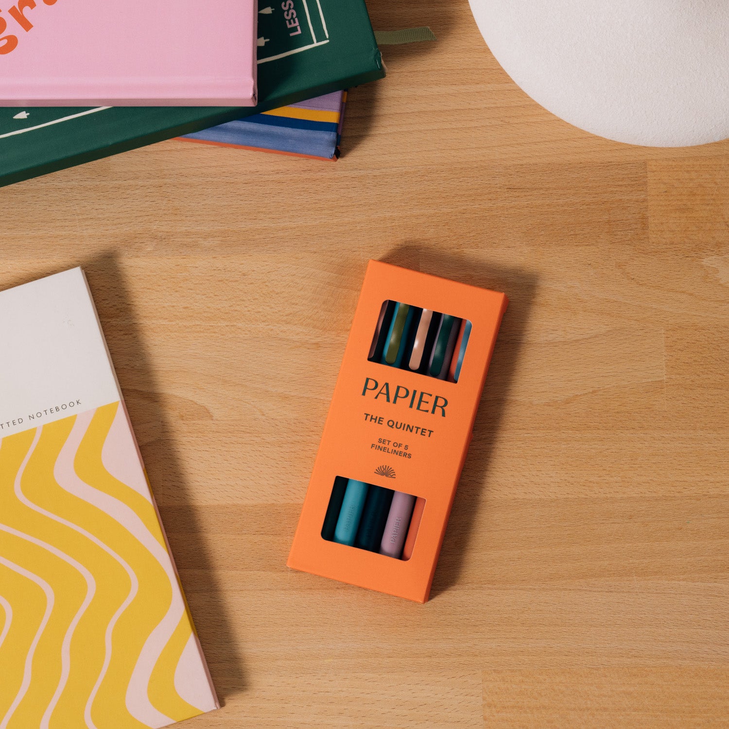 Papier Quintet Fineliner Set in its orange box on a desk with notebooks