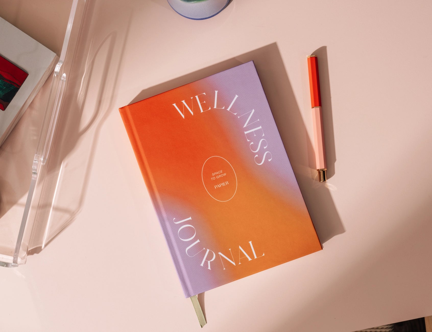 Papier Warmth Wellness Journal on a pink desk with a candle and pen