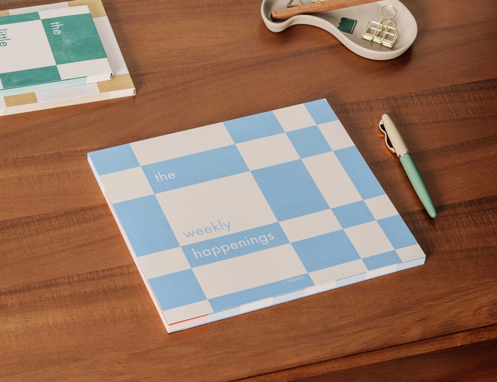 Papier Weekly Happenings List Pad on a wooden desk with a pen and notebooks, cover view
