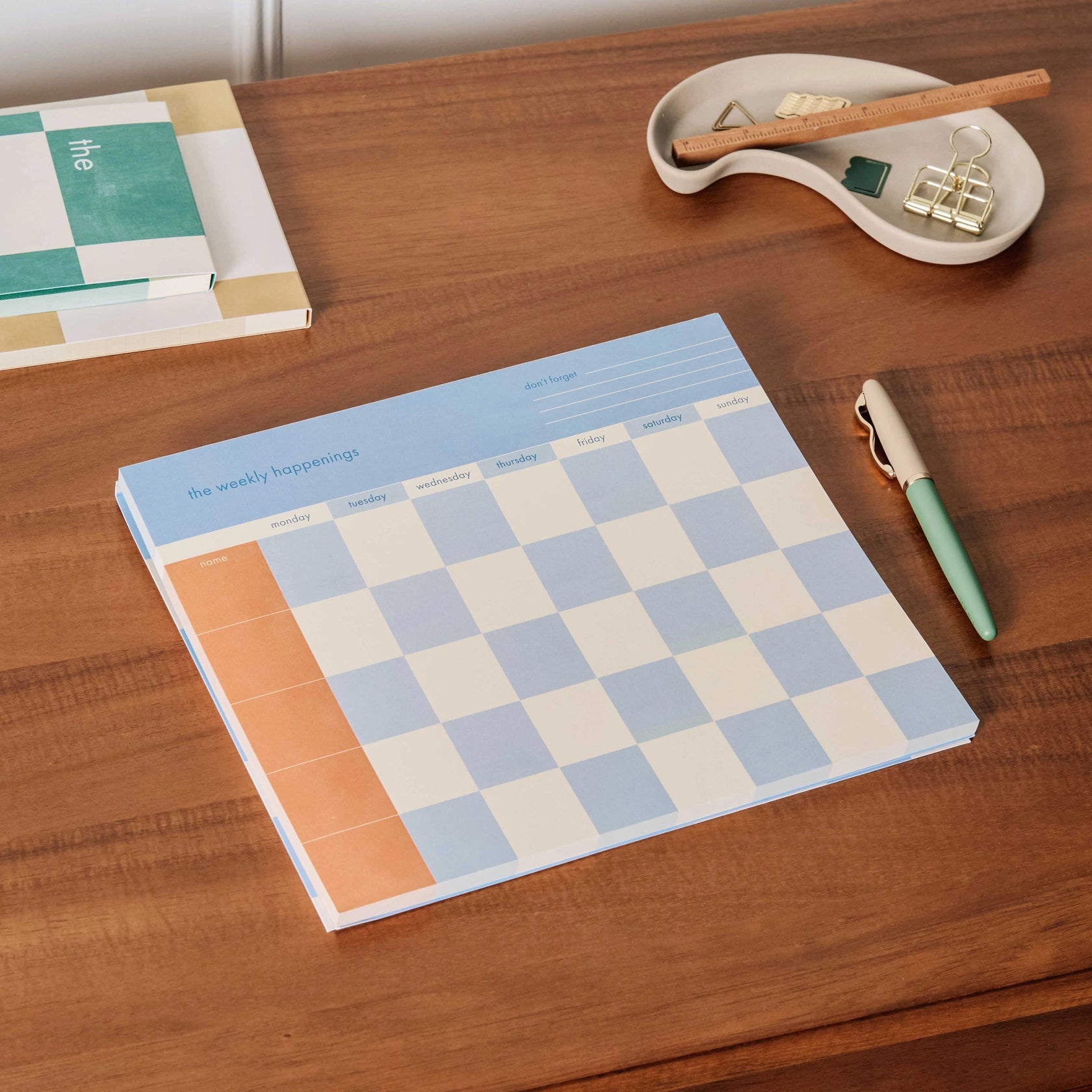 Papier Weekly Happenings List Pad open to a weekly page on a wooden desk with a pen