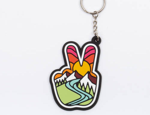 Peace sign keychain, a hand making a peace sign filled with a sunburst, snowy mountains and a green river valley, on a silver split ring.