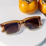 Peepers Airplane Mode Sunglasses in Golden Ombre on a white plate beside orange persimmons