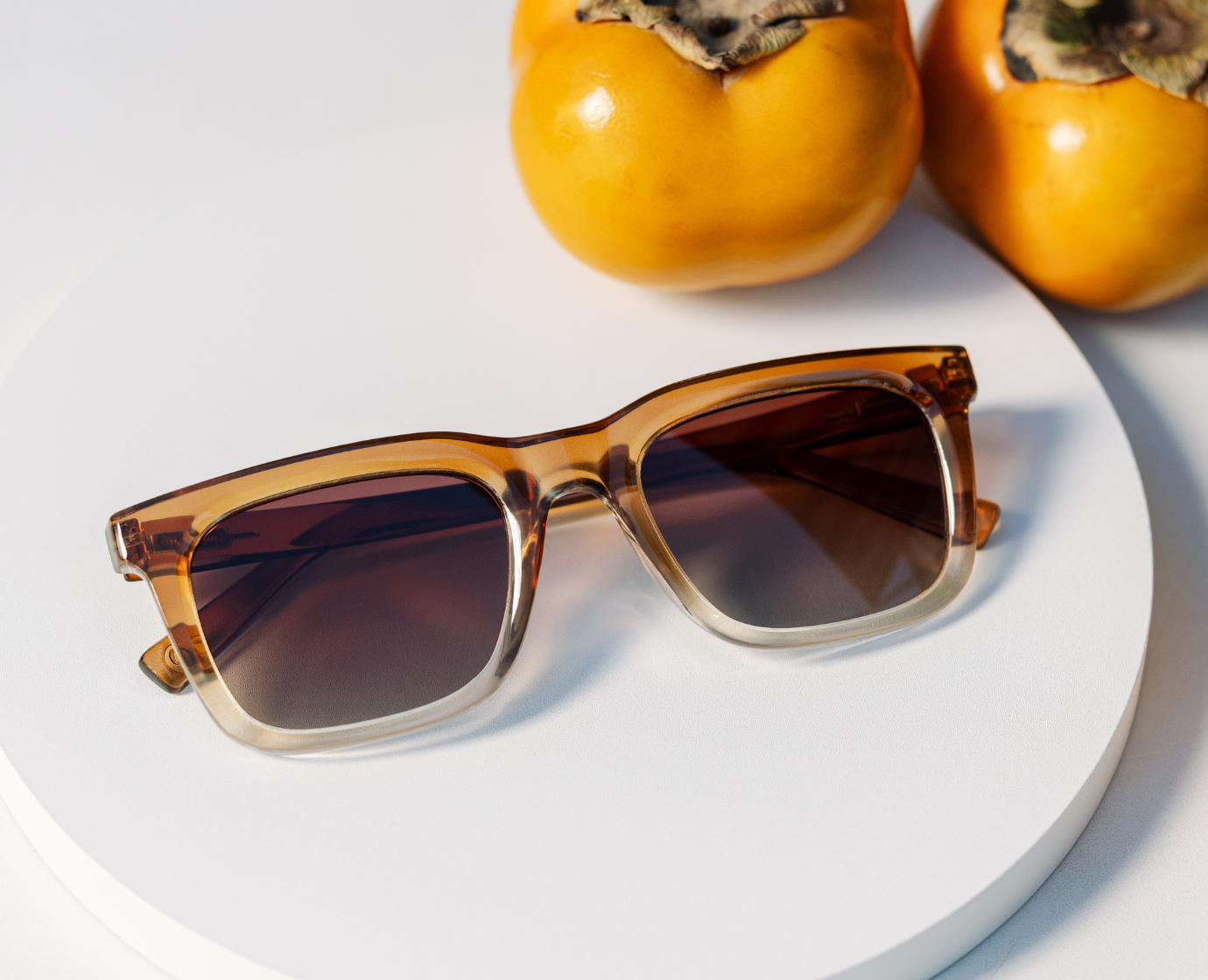 Peepers Airplane Mode Sunglasses in Golden Ombre on a white plate beside orange persimmons