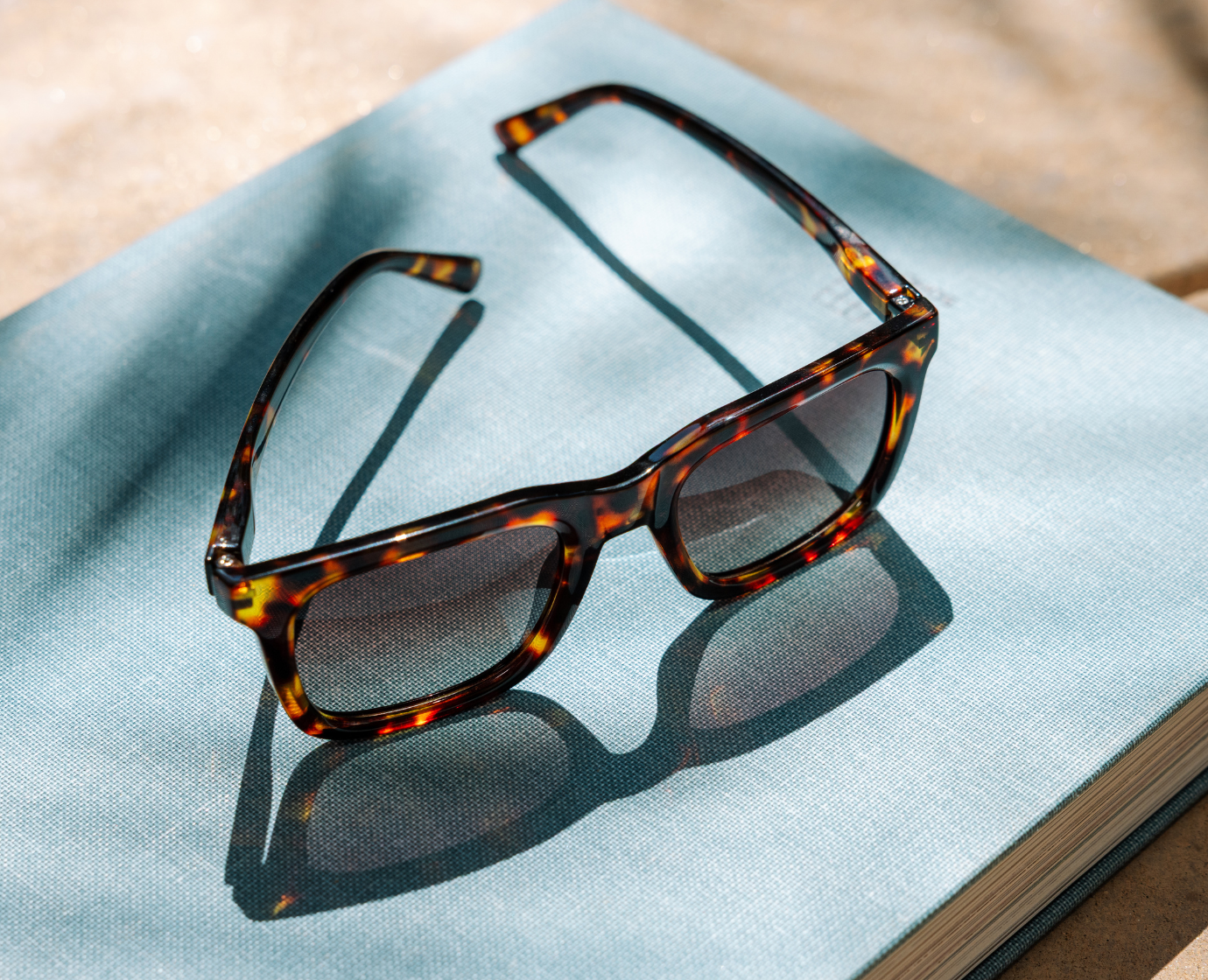 Peepers Airplane Mode Sunglasses in tortoise resting on a blue linen cloth in sunlight