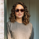 Peepers Airplane Mode Sunglasses in tortoise worn by a curly-haired woman in a taupe sweater in a doorway