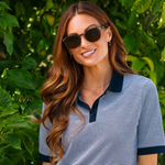 Smiling woman with long brown hair wearing Peepers Boho II Sunglasses in Brown outdoors by green foliage