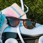 Peepers Boho II Sunglasses in Brown resting on a pair of light blue roller skates in the grass