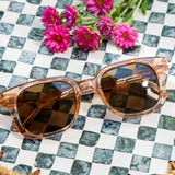 Peepers Clubhouse Sunglasses in Blush on a green checkered surface with pink flowers