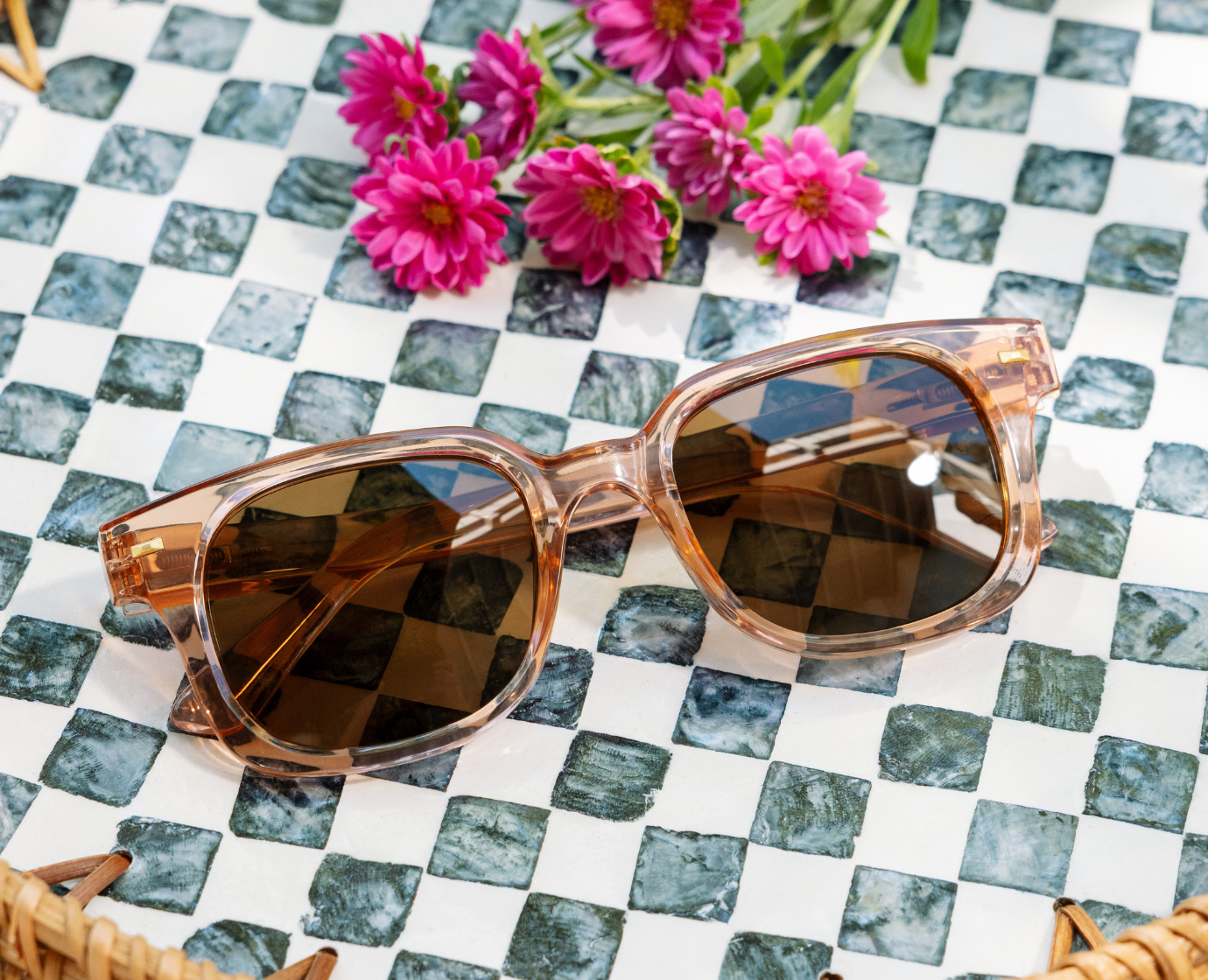 Peepers Clubhouse Sunglasses in Blush on a green checkered surface with pink flowers