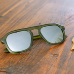 Peepers Deep Dive Sunglasses in olive green resting on a wooden table